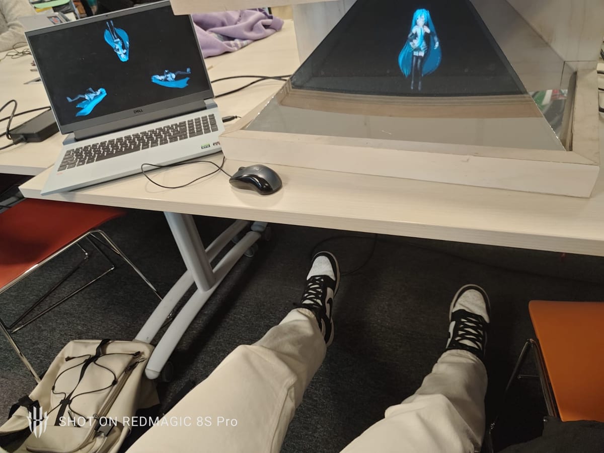 A laptop showing the Figma control view next to the pyramid, a blue figure floating inside